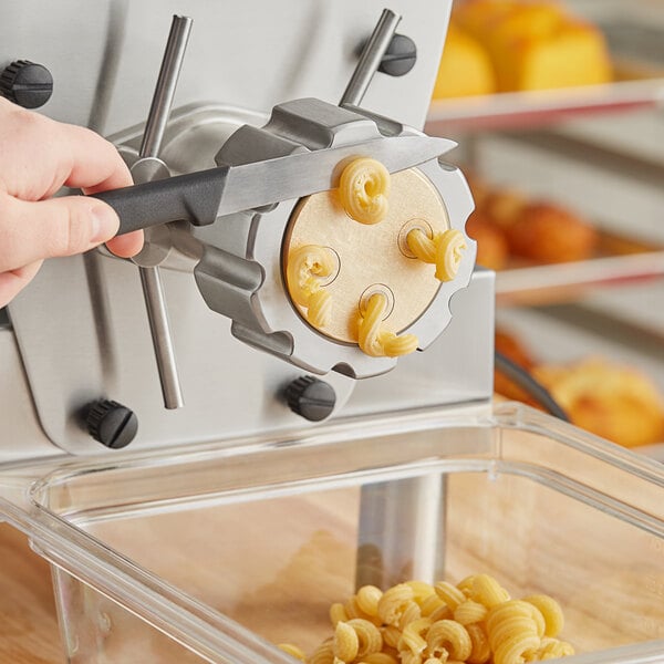 A hand using a black Estella Cavatappi pasta die to cut pasta.