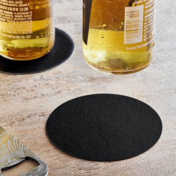 A pair of beer bottles on a Hoffmaster black pulpboard coaster.