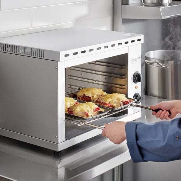 A person using an Avantco countertop cheese melter to cook food in a pan.