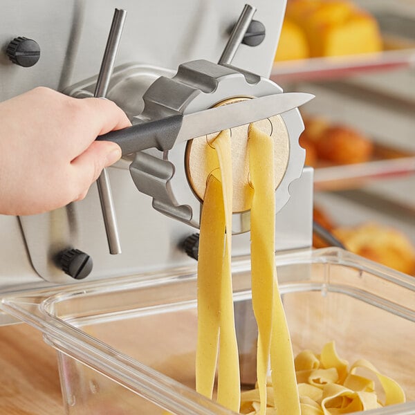 A hand using a yellow and white handle to cut pasta with a round yellow #38 Pappardelle pasta die.