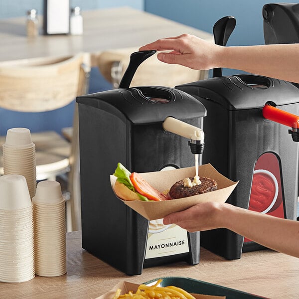 A person using a black ServSense mayonnaise pouch dispenser to pour liquid onto a burger.