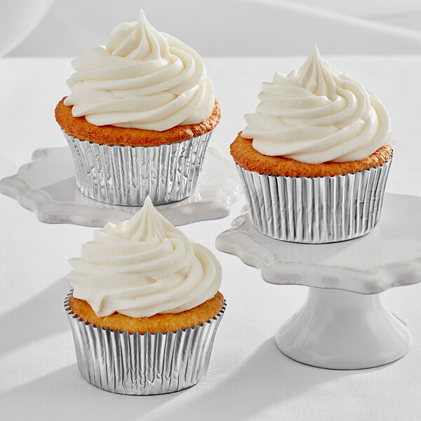 Three Enjay silver foil baking cups with cupcakes with white frosting.