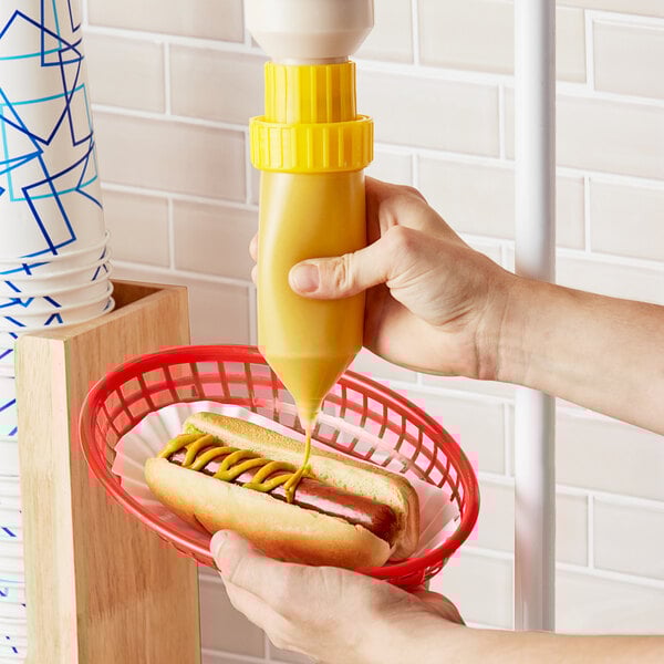 A person using an Asept hanging condiment pump to dispense mustard onto a hot dog.