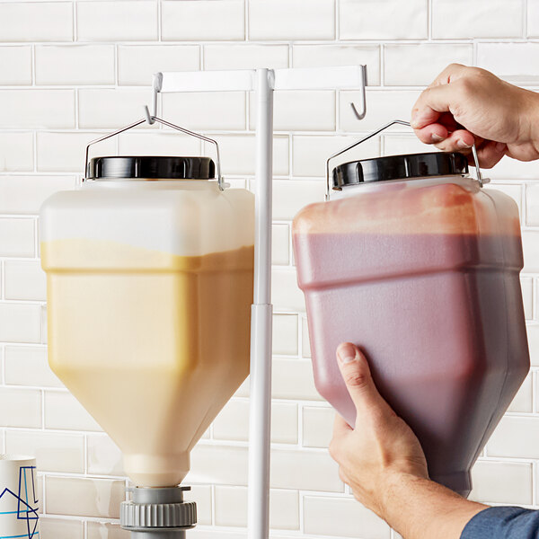 A hand using an Asept countertop stand to dispense liquid from a hanging container.