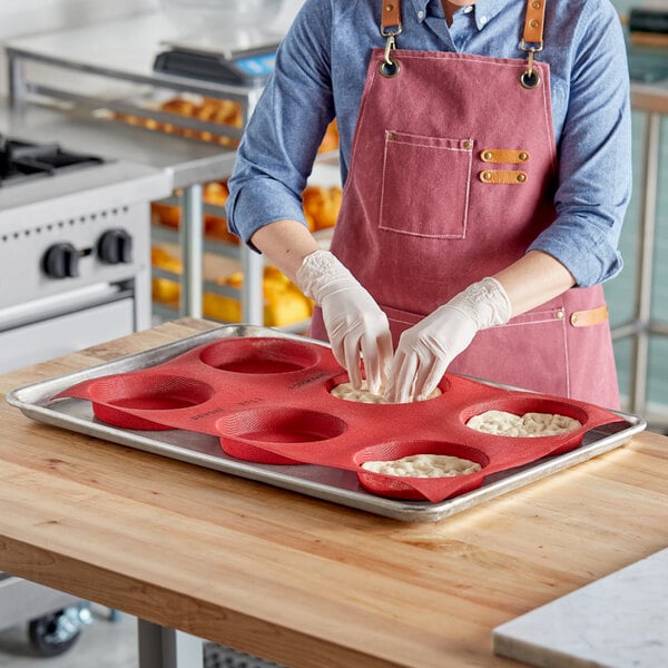 A woman in a pink apron using a Pavoni silicone bread and pastry mold to make white dough in a professional kitchen.