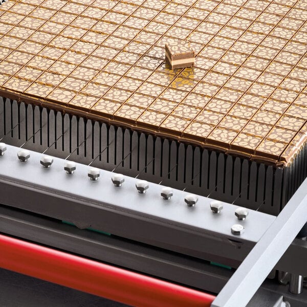 A Pavoni candy slicer cutting chocolate on a grid.