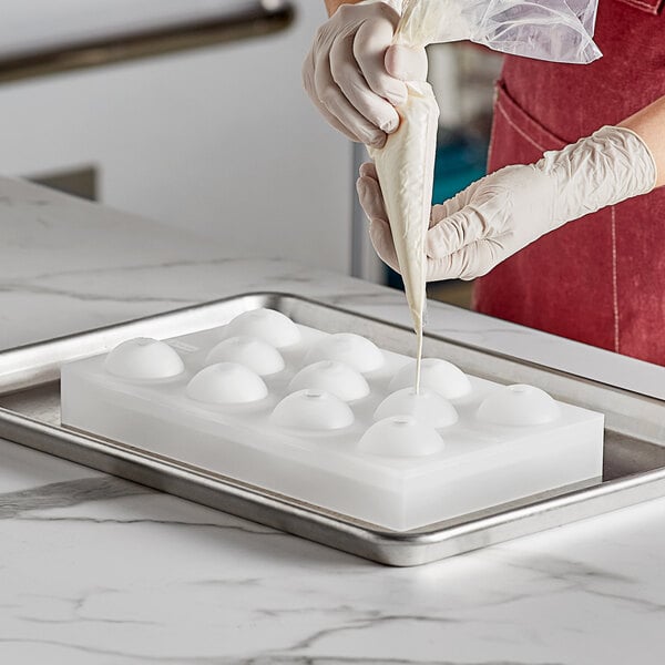 A woman using a Pavoni silicone chocolate mold to make white round chocolate spheres.