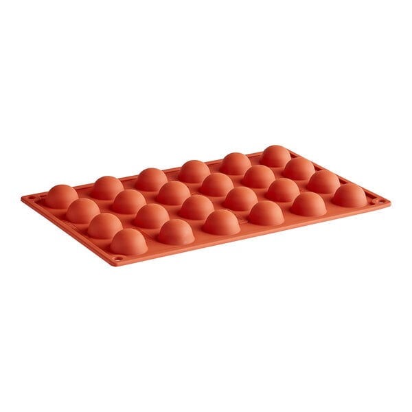 A close-up of a round orange silicone baking mold with 24 small round cavities.