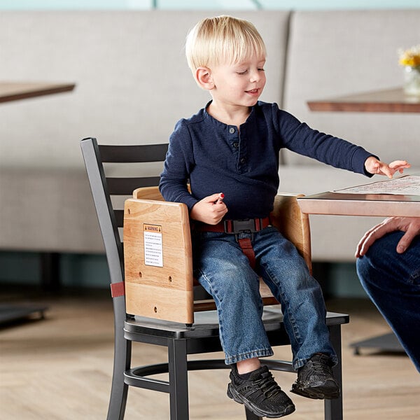 A child sitting in a Lancaster Table & Seating wooden booster seat at a table.