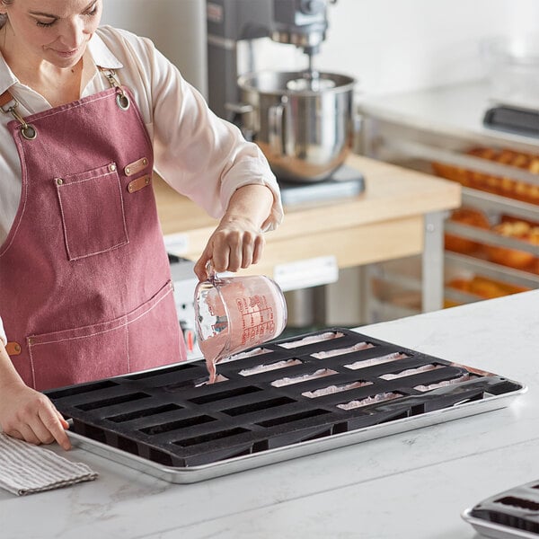 A woman in a pink apron pouring liquid into a black Pavoni Pavoflex silicone baking mold.