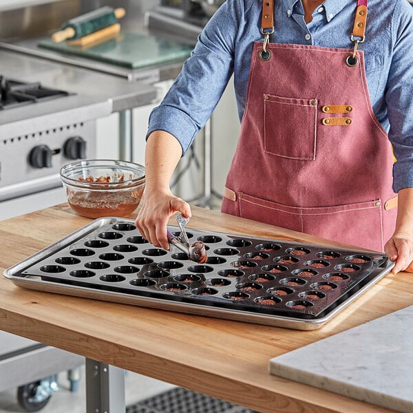 A woman in an apron using a spoon to fill a Pavoni Pavoflex mini muffin silicone baking mold on a marble counter.