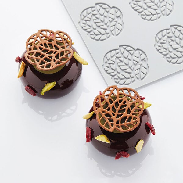 A white Pavoni silicone baking mold with leaves on it filled with chocolate-covered desserts.
