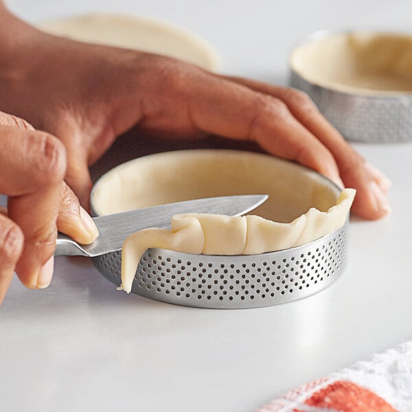 A hand using a knife to cut a tart baked in a Pavoni stainless steel tart ring.