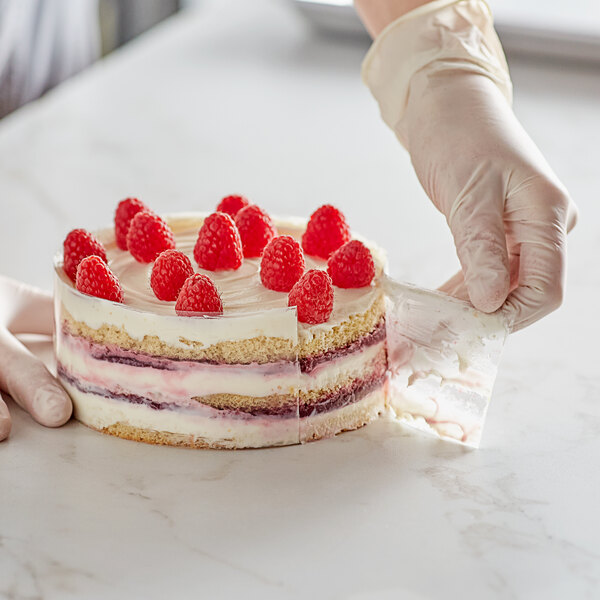 A hand wearing a white glove cutting a cake with raspberries using a Pavoni PVC cake collar.