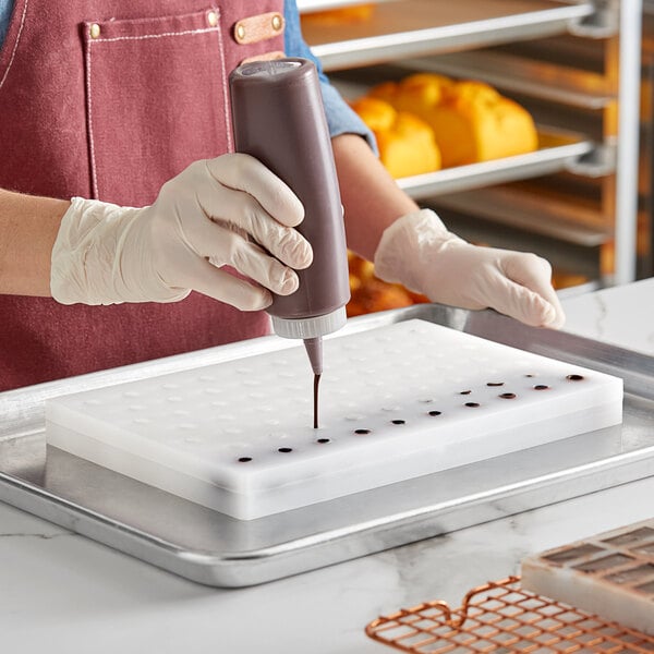 A person using a pastry bag to fill a Pavoni Chocoflex sphere chocolate mold with chocolate.