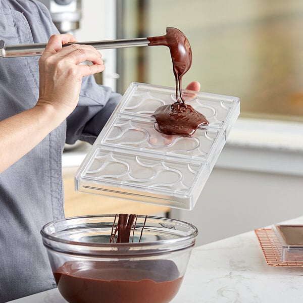 A person using a Pavoni polycarbonate chocolate bar mold to pour chocolate.