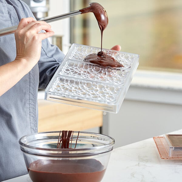 A woman using a Pavoni sparkling chocolate bar mold to pour chocolate on a tray.