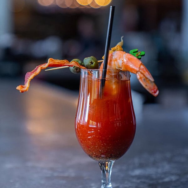 A glass of Bloody Mary garnished with a shrimp, bacon, olives, and a black jumbo straw.