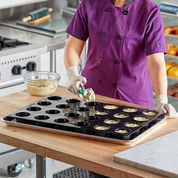 A woman in a purple apron using a Pavoni Pavoflex silicone muffin pan to make muffins.