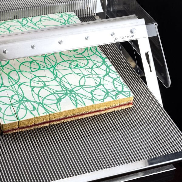 A Pavoni Lira semi-automatic dessert slicer cutting a cake with green swirls.