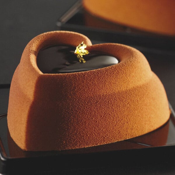 A heart shaped dessert with a gold leaf on a brown plate.