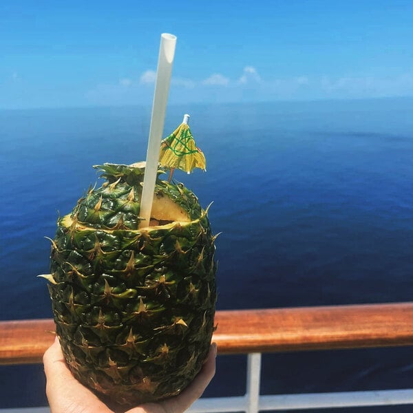 A natural wrapped giant straw inserted into a hollowed-out pineapple drink with a small decorative umbrella.
