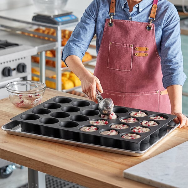 A woman in an apron pouring batter into a Pavoni silicone muffin tin.