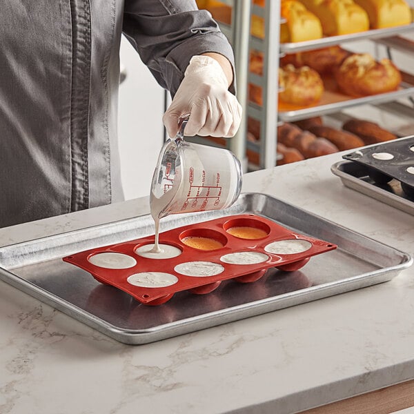 A person pouring batter into a Pavoni round silicone baking mold with 8 compartments.