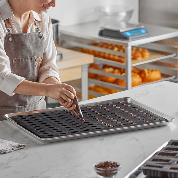 A person wearing an apron using a Pavoni Pavoflex quenelle silicone baking mold to make chocolate quenelles.