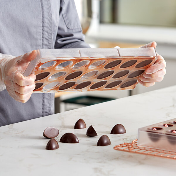 A woman holding a Pavoni Praline candy mold tray filled with chocolates.