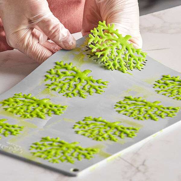 A person's hand holding a Pavoni Gourmand coral silicone baking mold filled with green batter.