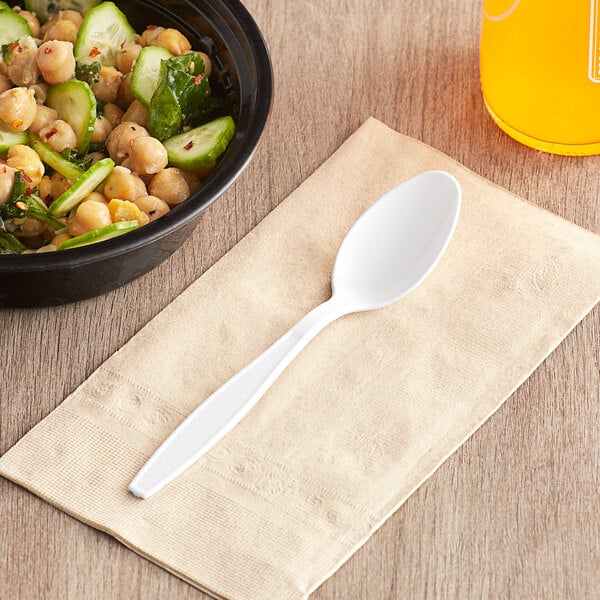 A bowl of food on a table next to a Choice white heavy weight plastic teaspoon.