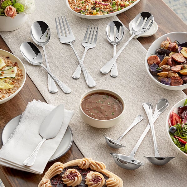 A table set with Acopa Swirl stainless steel serving utensils and plates of food.