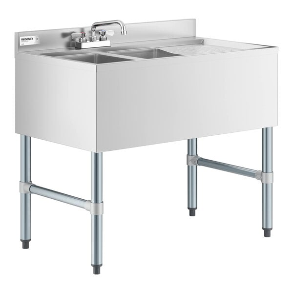 A stainless steel sink unit with two bowls, a right-side drainboard, a backsplash, and a faucet, supported by four metal legs.