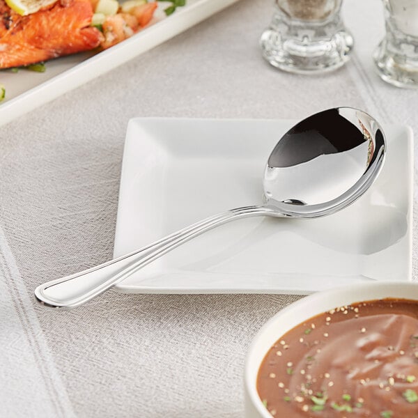 An Acopa Edgeworth stainless steel gravy ladle on a plate with brown gravy.