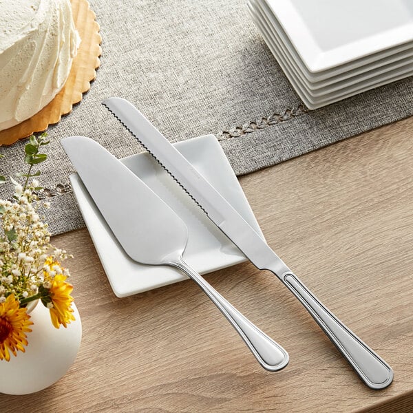 An Acopa Edgeworth stainless steel cake knife and fork on a white plate on a table with flowers.