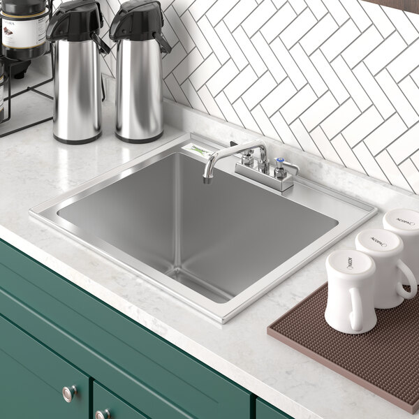 A Regency stainless steel drop-in sink with a faucet in the middle and coffee mugs and containers above it.