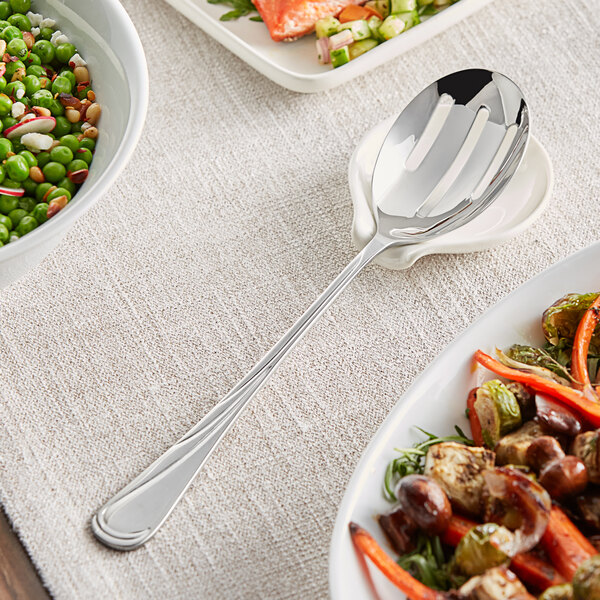 An Acopa stainless steel slotted serving spoon on a plate of vegetables.