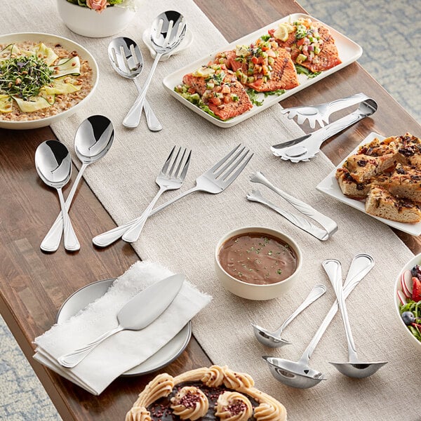 A table with plates of food and Acopa Swirl stainless steel serving utensils.