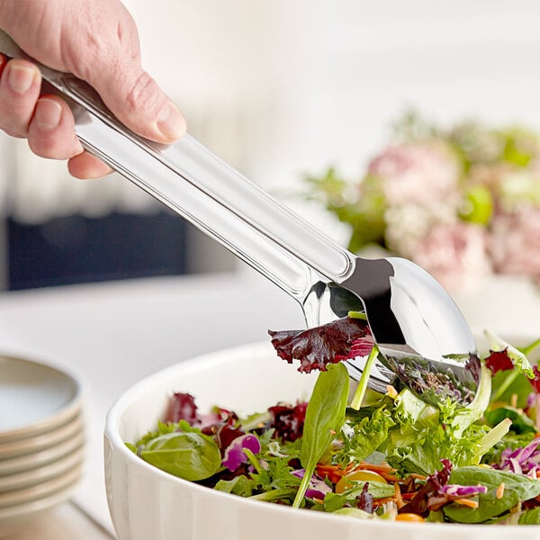 A hand using Acopa Edgeworth stainless steel serving tongs to serve salad