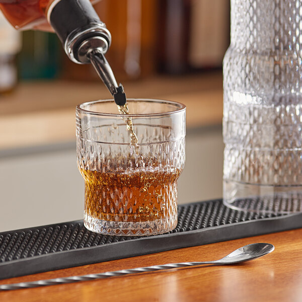 A person pouring whiskey into an Acopa stackable rocks glass on a counter in a cocktail bar.