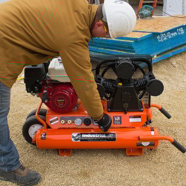 A man wearing a hard hat working on an Industrial Air Contractor wheelbarrow air compressor.