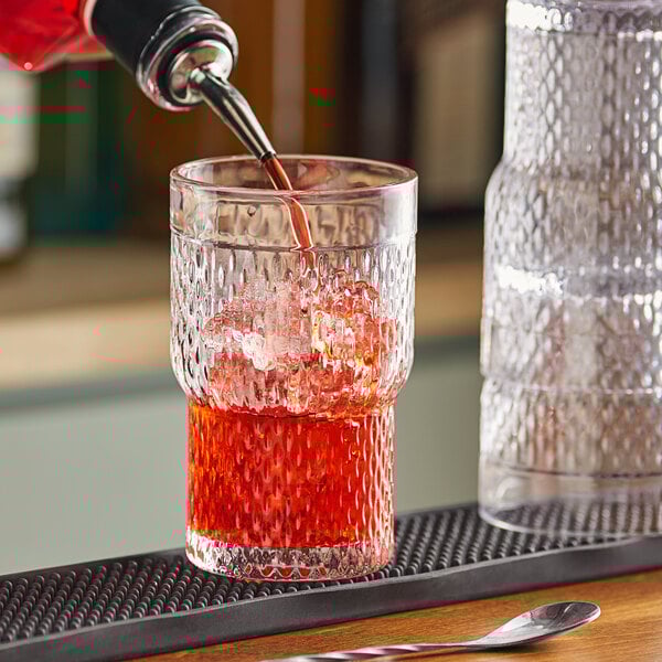 A person pouring a red drink into an Acopa Rivulet stackable beverage glass.