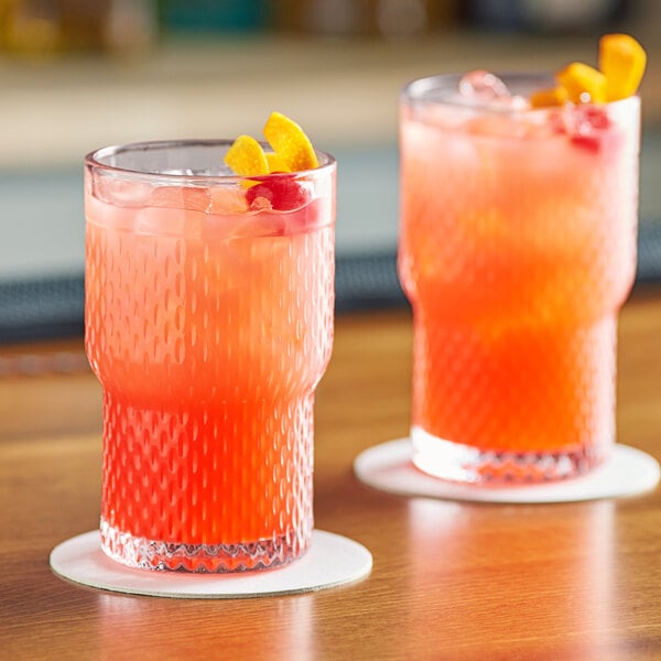 Two Acopa stackable beverage glasses filled with red liquid and ice with orange slices on a table.