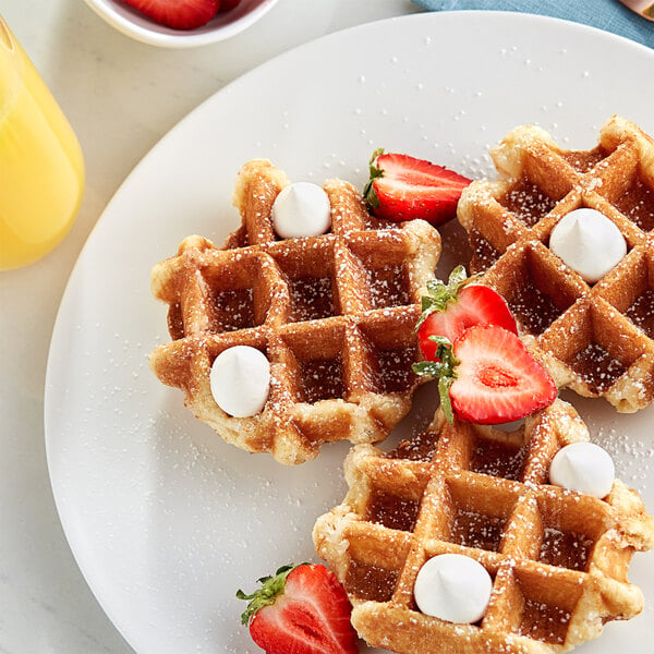 White Toque Heritage Liege waffles with strawberries and whipped cream on a white plate with a drink in the background.