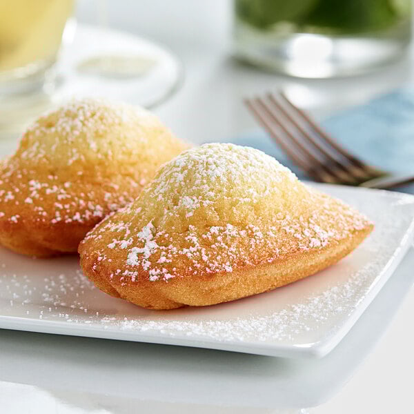 Two White Toque individually wrapped madeleines on a white plate with a fork.