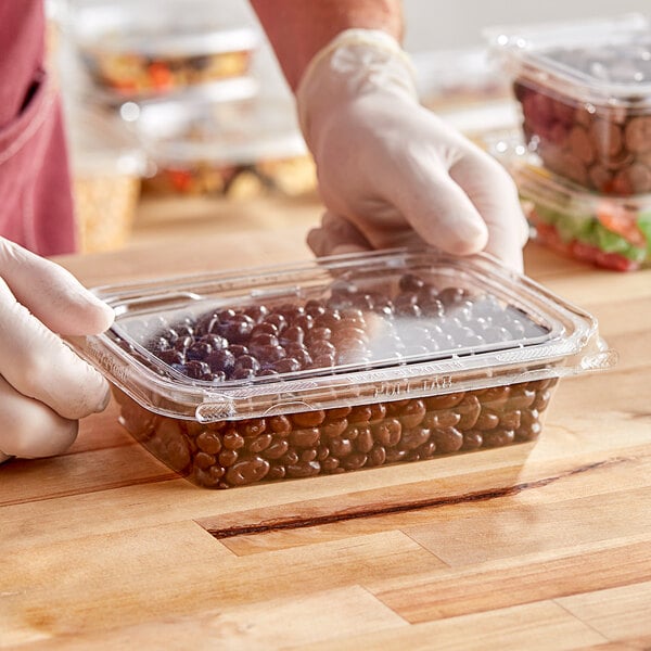 A gloved hand holding an Inline Plastics rectangular plastic container of beans.