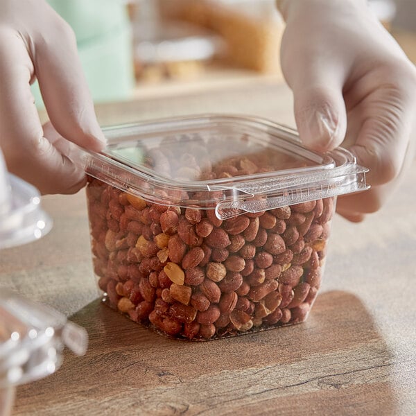 A person's hand holding an Inline Plastics Safe-T-Fresh plastic container of peanuts.