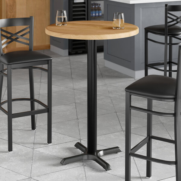 A Lancaster Table & Seating round bar table with a maple finish and two black chairs.