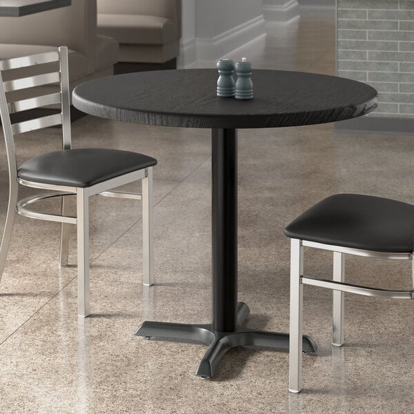 A Lancaster Table & Seating round table top with black wood finish on a table with two chairs.